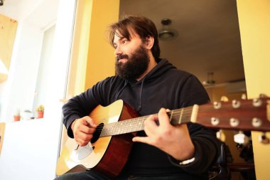 Mutlu sakallı adam evde akustik gitar çalıyor..