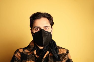 Siyah tıbbi maskeli genç adam. Sarı arkaplan.