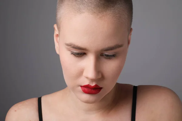 Primer plano de mujer joven con peinado afeitado, posando sobre fondo gris. —  Fotos de Stock