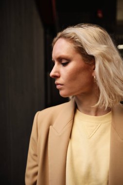 Bej takım elbiseli, dışarıda poz veren güzel bir genç kadının dikey portresi..