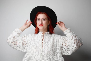 Beyaz duvarda poz veren kızıl saçlı hoş bir genç kadın..