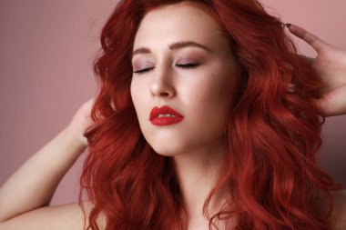 Pembe arka planda poz veren kızıl saçlı güzel bir genç kadın.. 