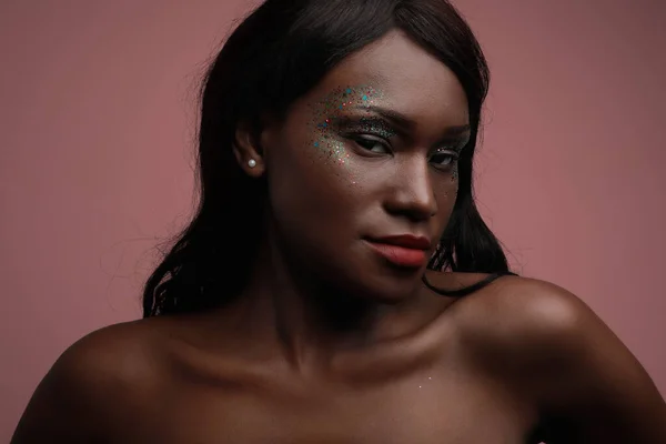 Portrait de jeune femme noire posant en studio, avec maquillage pailleté. — Photo