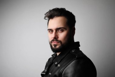 Yakışıklı genç manken portresi beyaz duvarda deri ceket giyiyor..