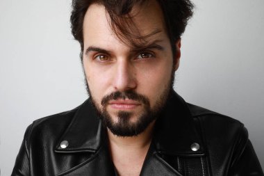 Yakışıklı genç manken portresi beyaz duvarda deri ceket giyiyor..