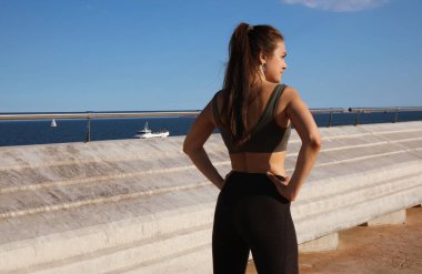 Spor kıyafetli genç bir kadının arka tarafta, dışarıda esneme egzersizi yaparken çekilmiş fotoğrafı..