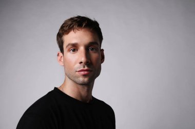 Gri duvarda izole edilmiş siyah tişörtlü genç adamın portresi..