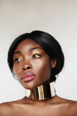 Stüdyoda poz veren altın makyajlı genç siyahi bir kadının dikey portresi.