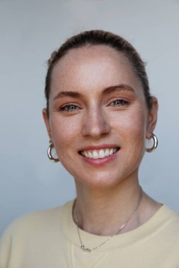 Beyaz duvarda gülümseyen mutlu bir kadının dikey görüntüsü, cilt bakımı ve sağlık.