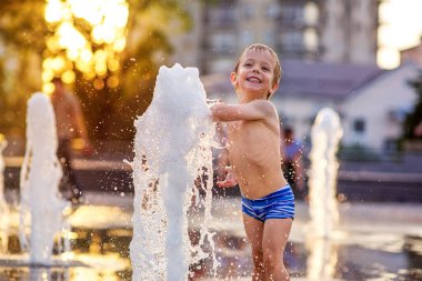 4 yaşında mayo ve timsah gibi giyinmiş bir çocuk çeşme suyuyla oynuyor, eğleniyor. Şehirde yaz.