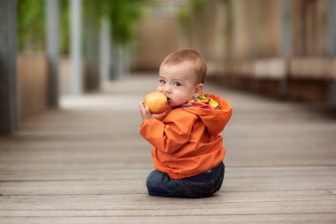 Sokakta yerde sürünen bir çocuk elinde bir elma tutuyor.