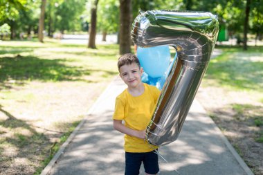 Sarı tişörtlü bir çocuk yedi numaralı formda büyük bir balon tutuyor. Çocukların doğum günü. Yedi yıl.