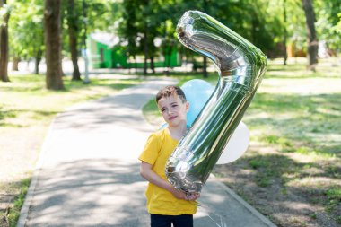 Sarı tişörtlü bir çocuk yedi numaralı formda büyük bir balon tutuyor. Çocukların doğum günü. Yedi yıl.