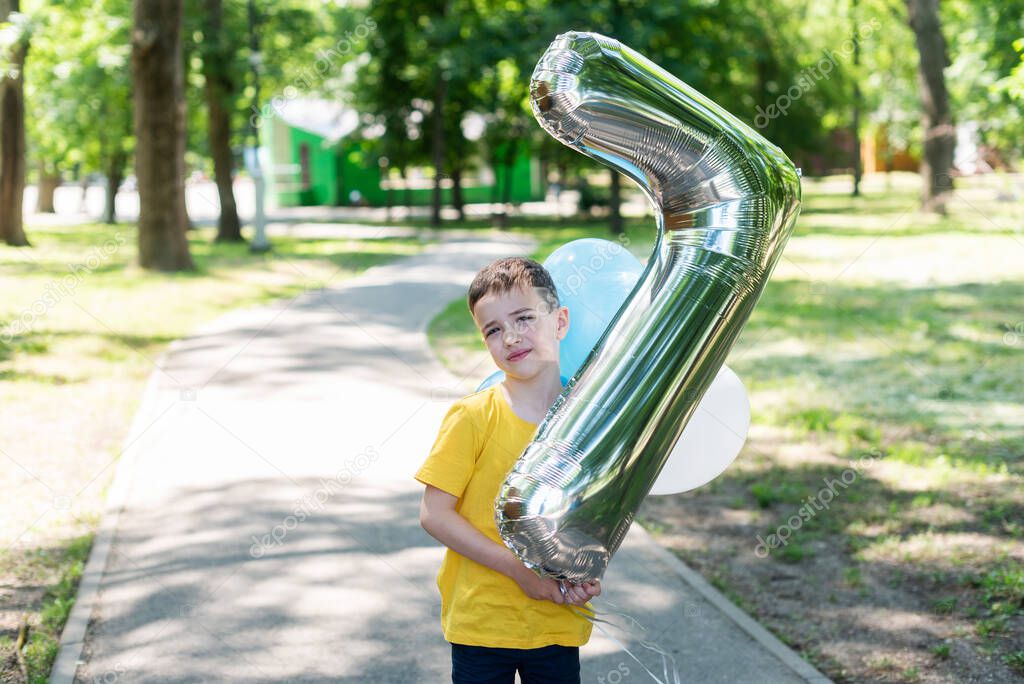 A boy in a yellow T-shirt is holding a large balloon in the form of the number seven. Children's birthday. Seven years