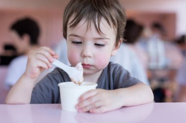 3-4 yaşlarında bir çocuk bir kafede dondurma yiyor. Yakın plan portre. Şehirde yaz mevsimi. Isı