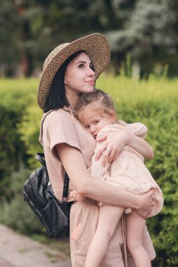 Genç bir anne küçük kızını kollarına alır ve ona bir şey söyler. Anneler Günü