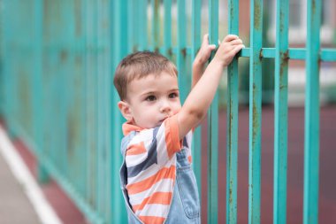 Çocuk parkında bir çocuk, uzun yeşil bir çit, boyalı bir eskrim..