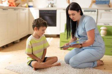 Mavi takım elbiseli güzel bir esmer kız terapist eğitim kartlarının yardımıyla eğitimde olan çocukla meşgul. Çocuk gelişimi