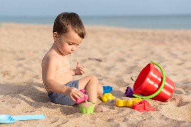 Sevimli çocuk kumsalda oyuncaklarla oynuyor. Yaz tatili