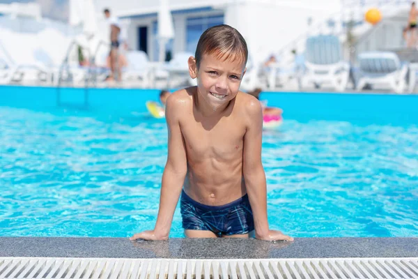 The boy on the side of the pool is smiling. The open air swimming pool.