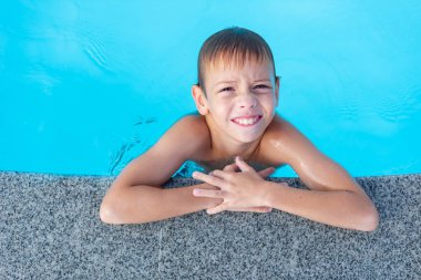 Havuzun kenarındaki çocuk gülümsüyor. Açık hava yüzme havuzu.