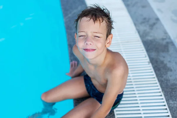 The boy on the side of the pool is smiling. The open air swimming pool.