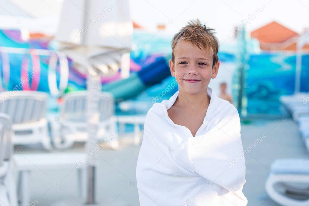 Close-up portrait of a smiling boy wrapped in a towel after swimming in the outdoor pool.