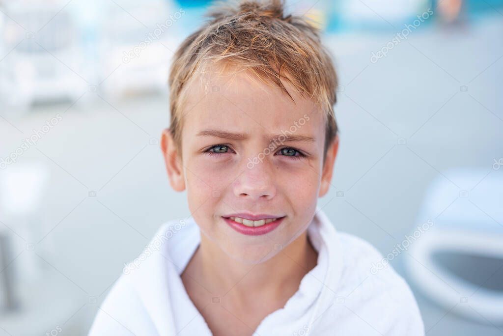 Close-up portrait of a smiling boy wrapped in a towel after swimming in the outdoor pool.