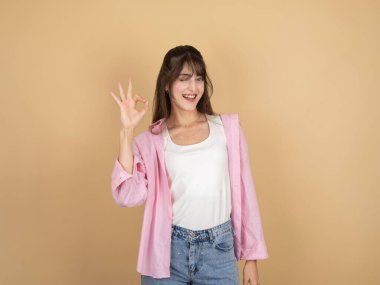 Kadın, tamam jest yap, genç beyaz, sevimli, güler yüzlü, esmer kadın bej arka planda izole edilmiş, mutlu yüz ifadesi göster..