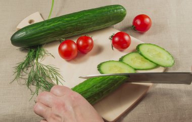 Vejetaryenlik. Bir salatalık tutan insan el kesme tahtası üzerinde domates