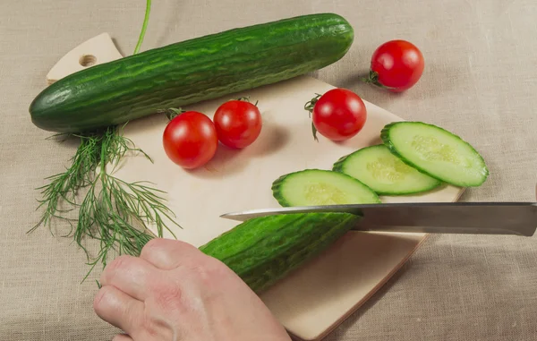 Vegetarianism. Mänskliga handen håller en gurka, tomat på cutting Board — Stockfoto