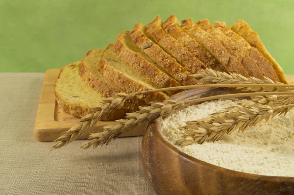 Нарезанный хлеб, мука в деревянной миске и колоски пшеницы — стоковое фото