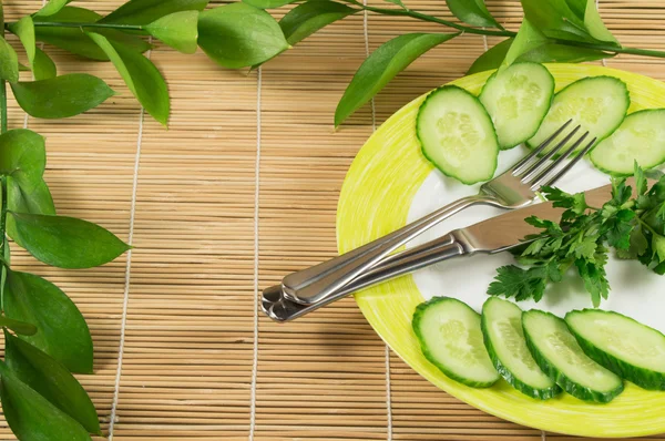 Skivad gurka med en kvist persilja på en tallrik. Begreppet viktminskning och kost. Bambu servett — Stockfoto