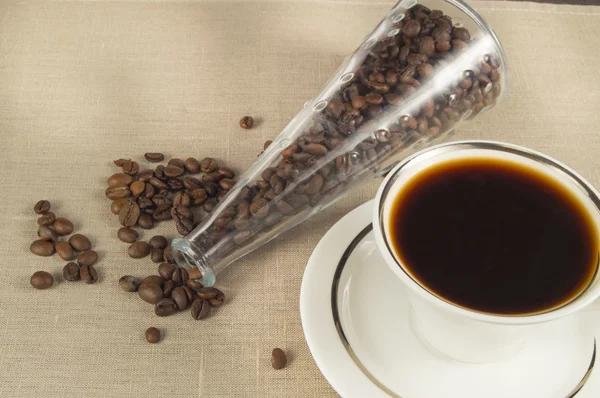 Roasted coffee beans in a glass bottle and a Cup of coffee on linen cloth — Stock Photo, Image