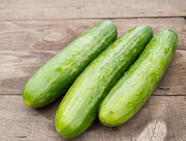 Three fresh cucumber lying on an old wooden background — Stock Photo, Image