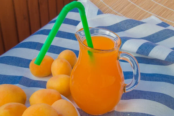 Suco de damasco em um jarro de vidro com palha e frutas em guardanapo — Fotografia de Stock