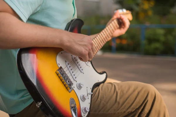 Young man hipster sitting playing guitar, close-up — Stock Photo, Image