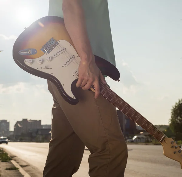 Young man standing with a guitar on background of sky and sunlight — Stock Photo, Image