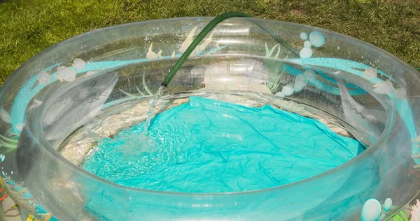 En plastbassäng är fylld med vatten från en gummislang en sommardag utomhus — Stockfoto