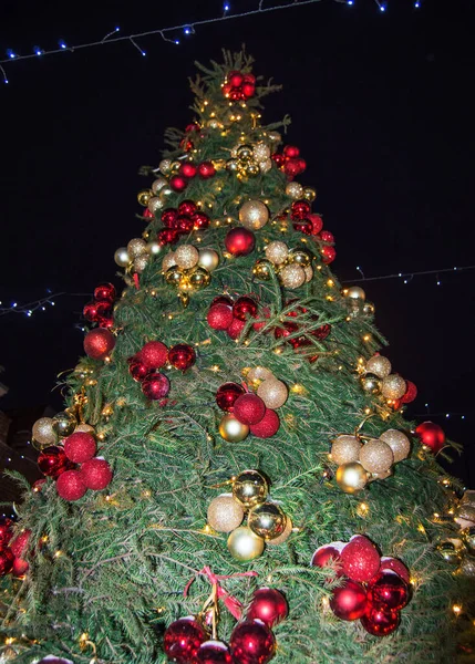 Árbol de Navidad ricamente decorado con luces multicolores y globos brillantes, al aire libre, contra el cielo nocturno de invierno oscuro, vista inferior, vertical — Foto de Stock