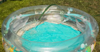 Plastik bir havuz, açık havada bir yaz gününde kauçuk bir hortumdan suyla doludur..