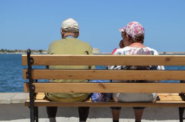 Yaşlı bir çift deniz kenarındaki bir bankta oturuyor ve deniz manzarasına hayran, arkadan manzaraya..