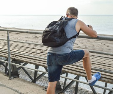 Sırt çantalı gezgin açık denizi seyrediyor, şafağı seyrediyor, siperlere yaslanıyor, özgürlük ve rahatlama konsepti..