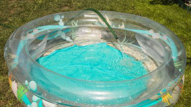 Plastik bir havuz, açık havada bir yaz gününde kauçuk bir hortumdan suyla doludur..