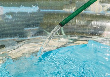 Yeşil plastik hortum yaz günü açık havuza su dökerek kapanır..