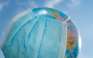 Mavi gökyüzüne karşı tıbbi maskeli bir küre. Dünya çapında bir salgın, Coronavirus 'a karşı koruma kavramı, açık hava, yaz.