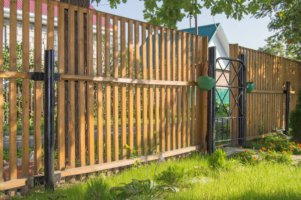 New wooden picket fence with metal gates, the concept of security and protection of a country house.