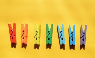 Gökkuşağının renklerine boyanmış yedi ahşap renkli mandal, sarı bir kağıtta, bir sırada uzanır..