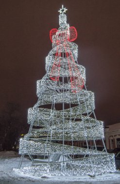 Metal inşaattan yapılmış şenlikli yaratıcı Noel ağacı. Parlayan lamba ışıkları var. Geceleri, açık havada..