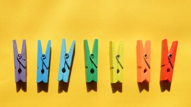 Gökkuşağının renklerine boyanmış yedi ahşap renkli mandal, sarı bir kağıtta, bir sırada uzanır..